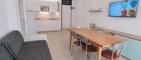 Un espacio habitable compacto con kitchenette, un comedor con mesa y sillas de madera, y un sofá.