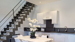 A modern kitchen with a dining area, featuring a staircase, white cabinets, and a wooden floor. - Chic & Central - Your Retreat in Le Mans (Le Mans)