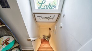 Una scala di legno con un cartello che recita 'Thankful' sopra, che conduce a una stanza con una finestra con la scritta 'Lake'.