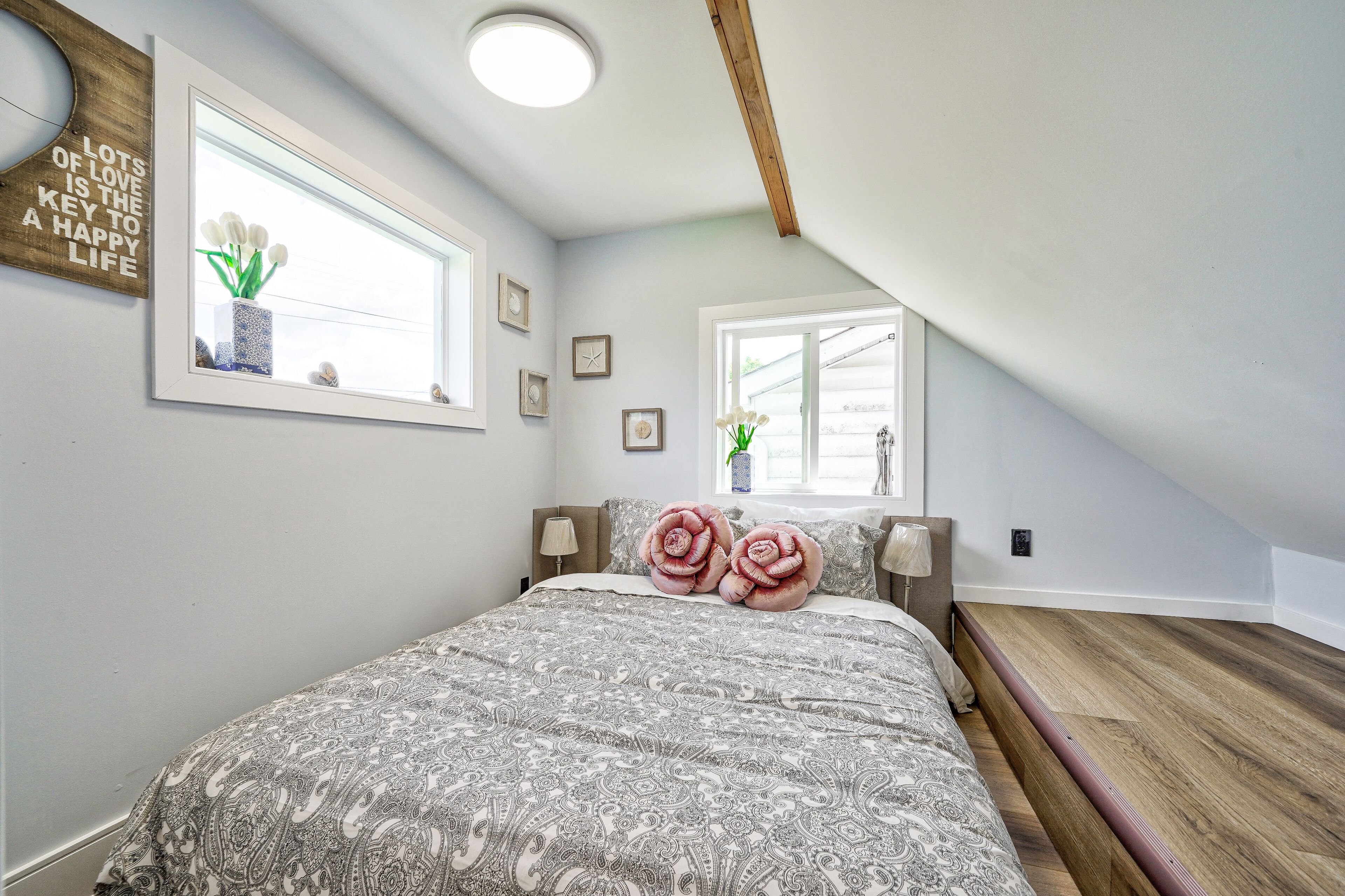 Ein Schlafzimmer mit einem großen Bett, zwei Fenstern und einem Holzbalken an der Decke.