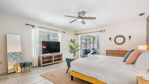A modern bedroom with a bed, a TV, a ceiling fan, and a large window.