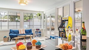 A cozy room with a blue sofa, a small table, colorful cupcakes, and a Pac-Man arcade machine.