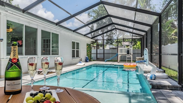 A pool area with a glass enclosure, a bottle of Moët & Chandon champagne, and a fruit platter.
