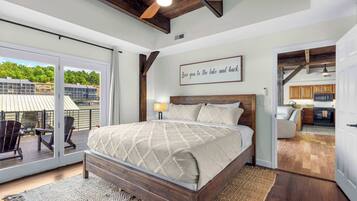 A bedroom with a large bed, a ceiling fan, and a view of a lake through a sliding glass door.