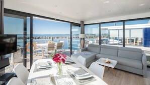 A modern, open-plan living area with a balcony overlooking a marina, featuring a dining table set, a sofa, and a TV. - Hausboot in Barth am Barther Bodden (Barth)