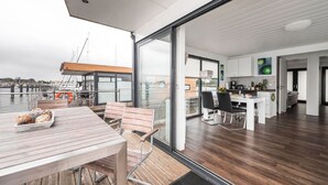 A modern interior with a wooden deck, a dining area, and a kitchen with large windows. - Hausboot in Barth am Barther Bodden (Barth)