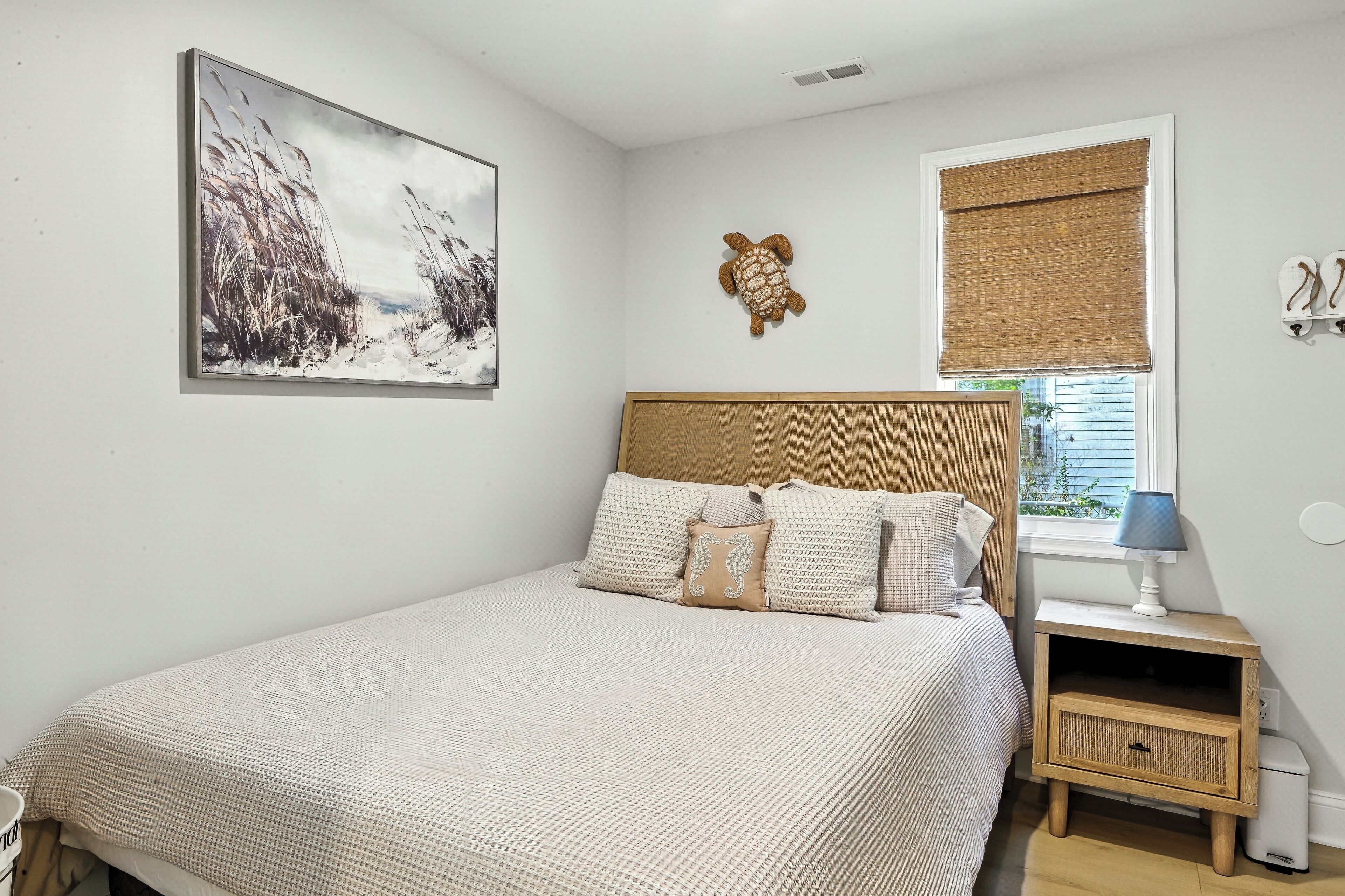 A bedroom with a bed, a nightstand, a wall-mounted turtle decoration, a window with a blind, and a framed picture on the wall.