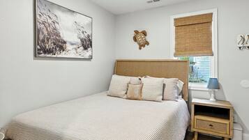 A bedroom with a bed, a nightstand, a wall-mounted turtle decoration, a window with a blind, and a framed picture on the wall.