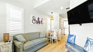 Een moderne woonkamer met een grijze bank, een houten eettafel en een bankje met blauw-witte kussens.
