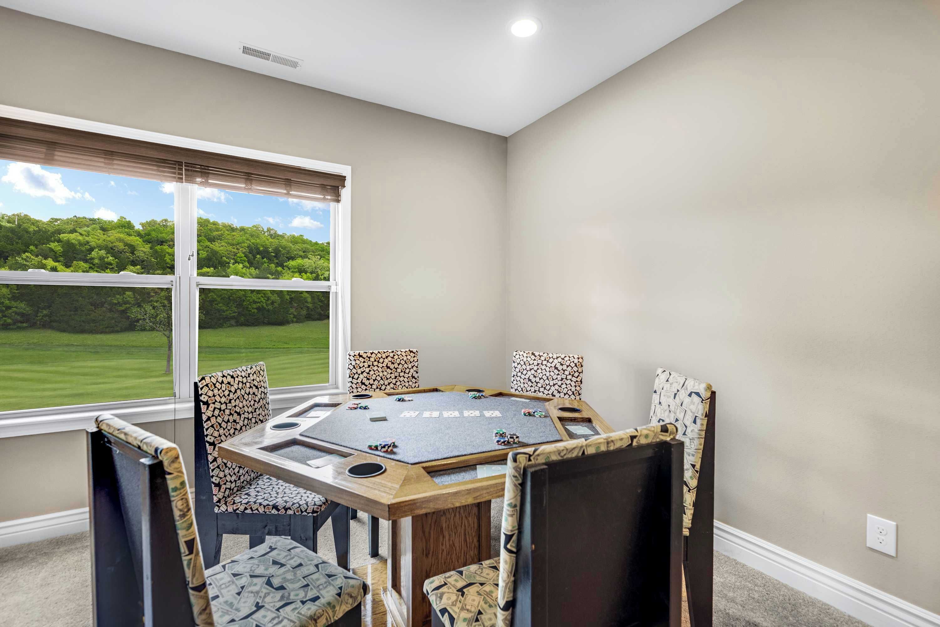 A room with a large window, a round table with chairs, and a view of a green landscape.