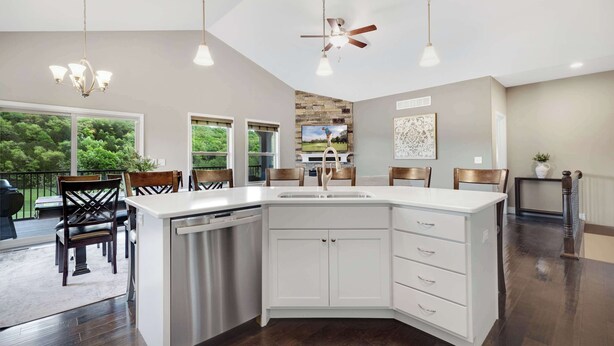 A modern kitchen with a large island, white cabinetry, and a built-in dishwasher. There are three pendant lights and a ceiling fan. - Fairway Lake Retreat (Camdenton)
