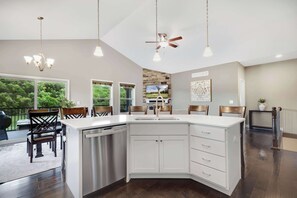 A modern kitchen with a large island, white cabinetry, and a built-in dishwasher. There are three pendant lights and a ceiling fan. - Fairway Lake Retreat (Camdenton)