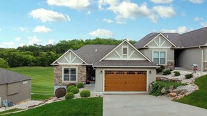 A two-story house with a stone facade, a wooden garage door, and a well-maintained lawn. - Fairway Lake Retreat (Camdenton)