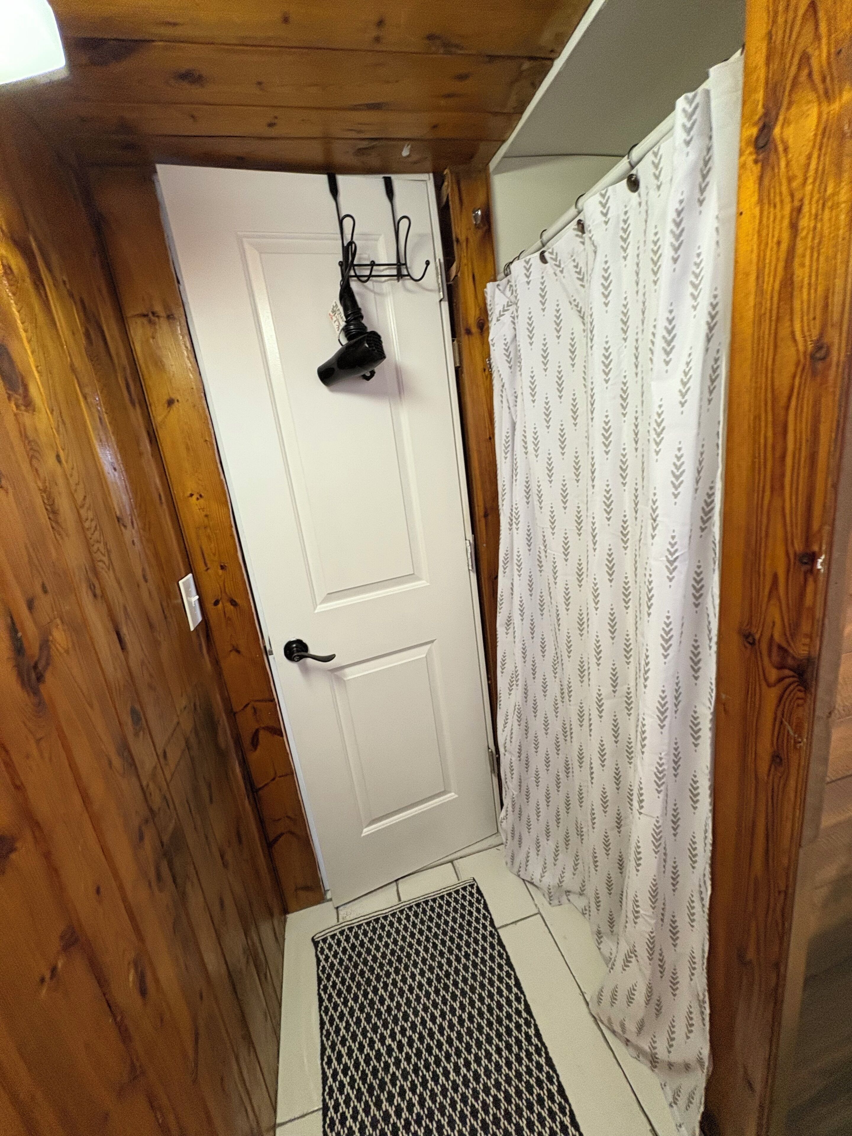A wooden interior with a white door, a shower curtain, and a black hairdryer on the wall.