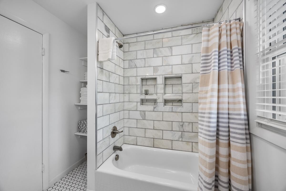A bathroom with a bathtub, a shower, and a striped shower curtain.