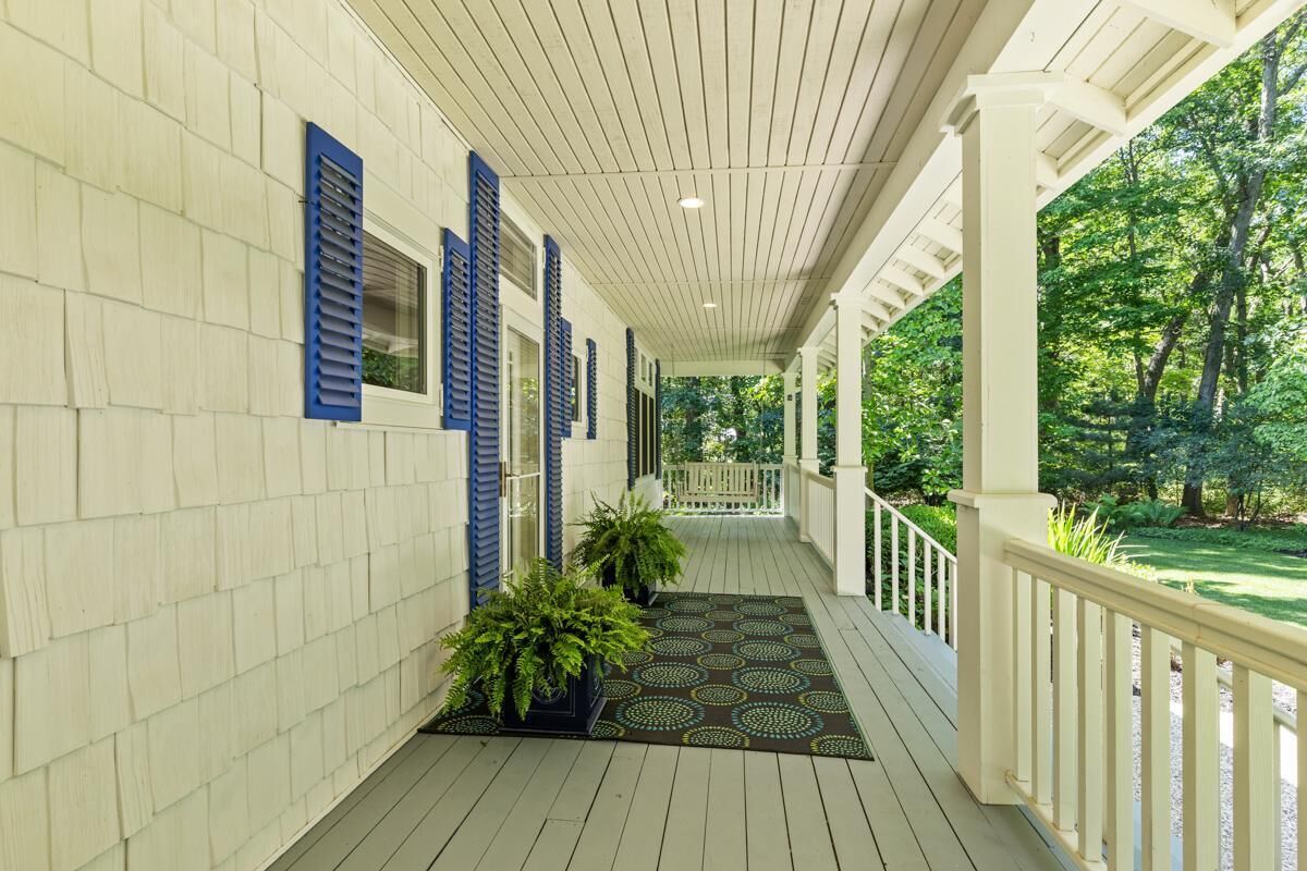 A covered porch with a wooden floor, white railings, and a view of a lush garden.