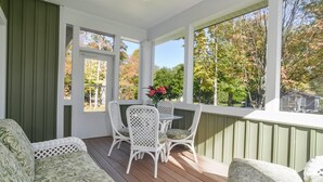 A covered porch with a table and chairs, large windows, and a ceiling fan. - Four Generations (Saugatuck)