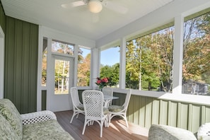 A covered porch with a table and chairs, large windows, and a ceiling fan.