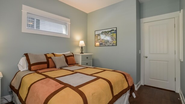 A bedroom with a bed, bedside table, lamp, window, and a door. - Four Generations (Saugatuck)