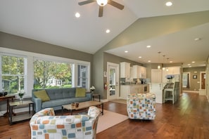 A spacious living room with a sofa and armchairs, a kitchen with white cabinets, and a dining area with a table and chairs.