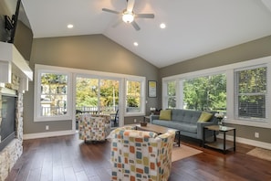 A spacious living room with a high ceiling, large windows, and a fireplace.
