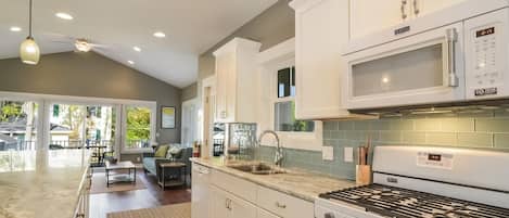 A modern kitchen with white cabinets, a stainless steel sink, a microwave, and a gas stove.