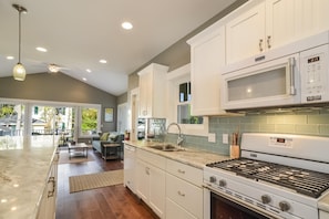 A modern kitchen with white cabinets, a gas stove, a microwave, and a large window.