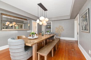 Uma sala de jantar moderna com mesa de madeira, cadeiras estofadas cinzentas e um lustre.
