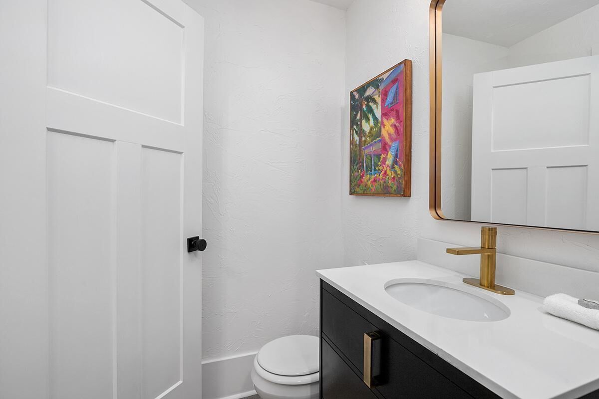 A bathroom with a white toilet, a sink with a gold faucet, and a mirror with a gold frame.