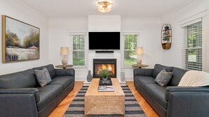 Ein modernes Wohnzimmer mit zwei schwarzen Ledersofas, einem Holztisch, einem Flachbildfernseher über einem Kamin und einem großen Landschaftsbild an der Wand.