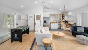 A modern living room with a foosball table, a sofa, a coffee table, and a kitchen area in the background. - Captains Cove and Crew Quarters (Douglas)