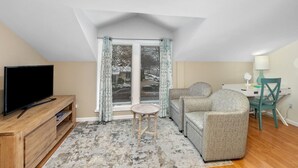 A cozy living room with a flat-screen TV, a sofa, a small round table, and a desk with a chair. - Downtown View (Saugatuck)