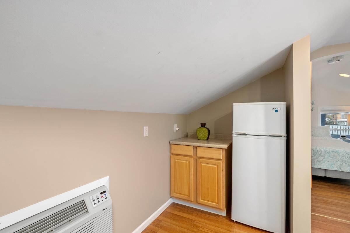 A compact kitchen with wooden cabinets, a white refrigerator, and a built-in air conditioner.