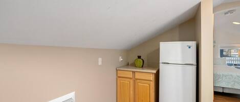 A compact kitchen with wooden cabinets, a white refrigerator, and a built-in air conditioner.