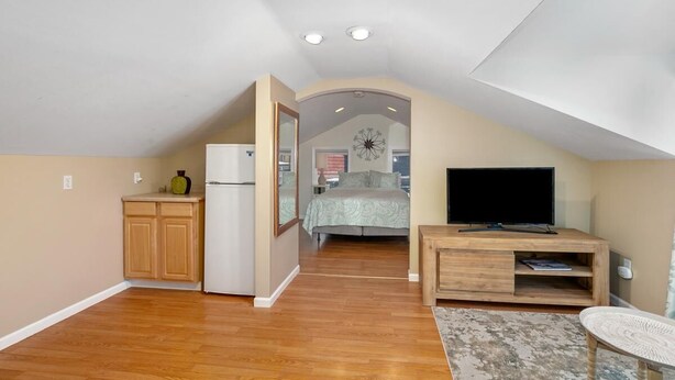 A compact living space with a kitchenette, a bedroom with a bed and a large window, and a TV on a wooden stand. - Downtown View (Saugatuck)