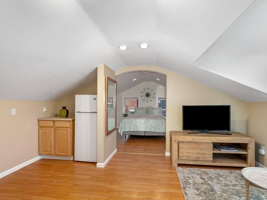 A compact living space with a kitchenette, a bedroom with a bed and a large window, and a TV on a wooden stand.