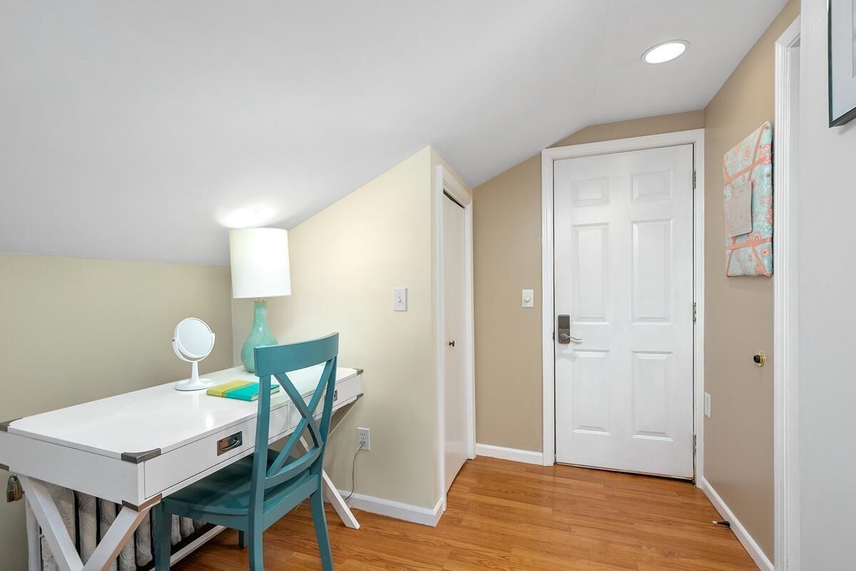 A small, well-lit room with a white desk, teal chair, and a white door.