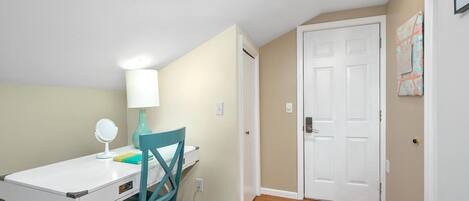 A small, well-lit room with a white desk, teal chair, and a white door.