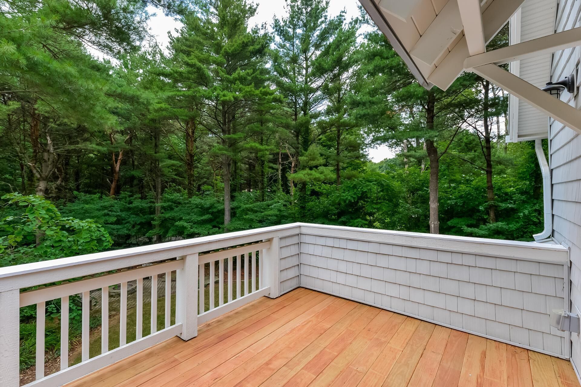 Une terrasse en bois avec des balustrades blanches donnant sur une zone boisée.
