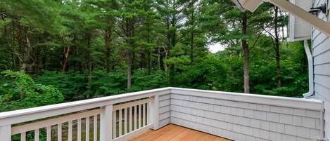 Une terrasse en bois avec des balustrades blanches donnant sur une zone boisée.