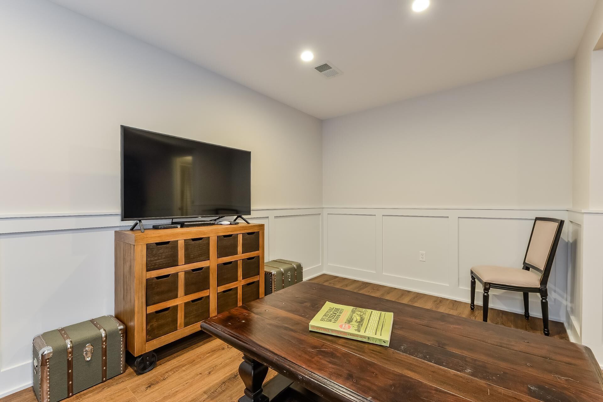 A room with a wooden table, a television mounted on the wall, a suitcase, and a chair.