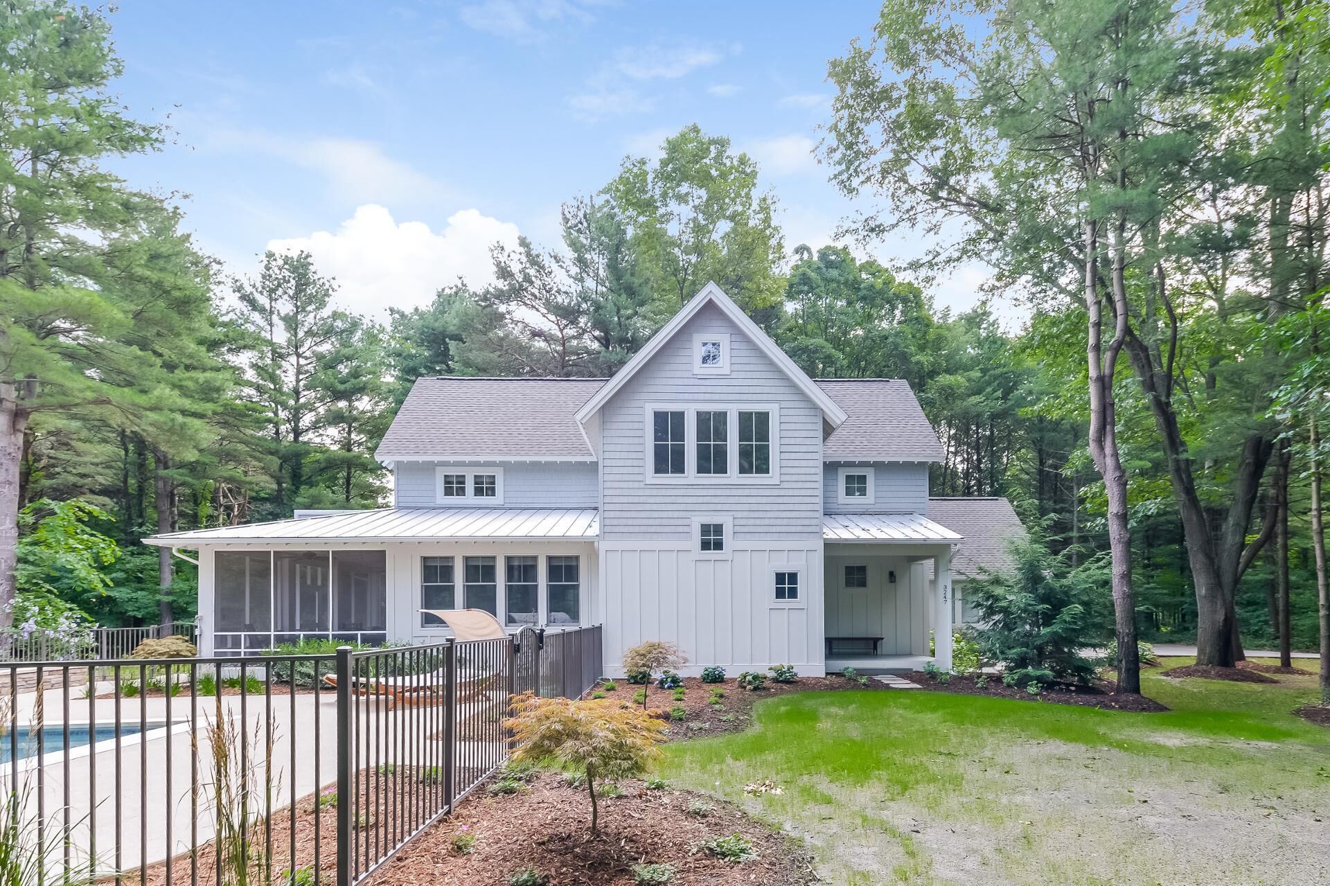 A two-story house with a large front porch, surrounded by trees and a fenced yard.