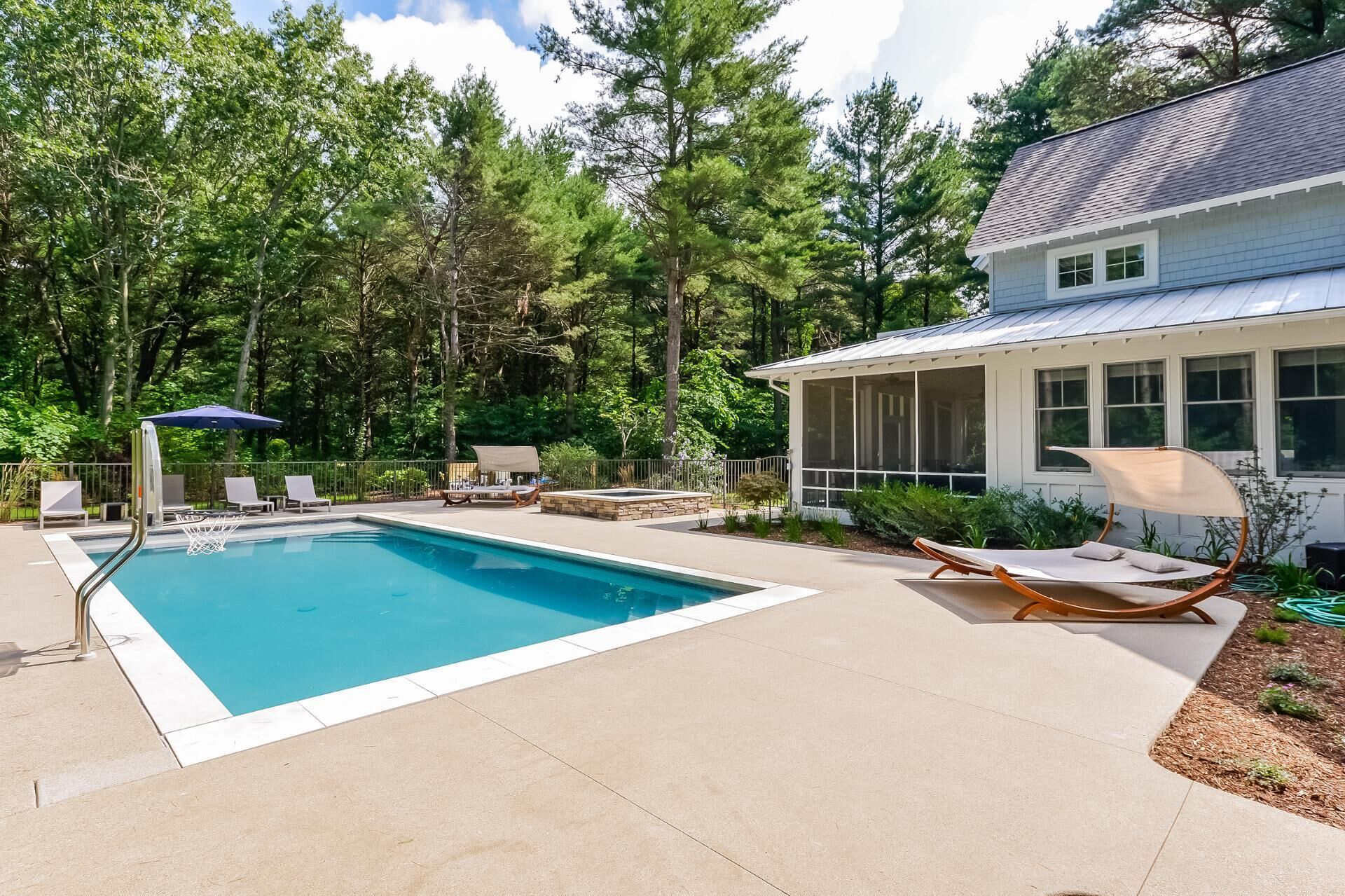 A backyard with a swimming pool, lounge chairs, and a house with large windows.