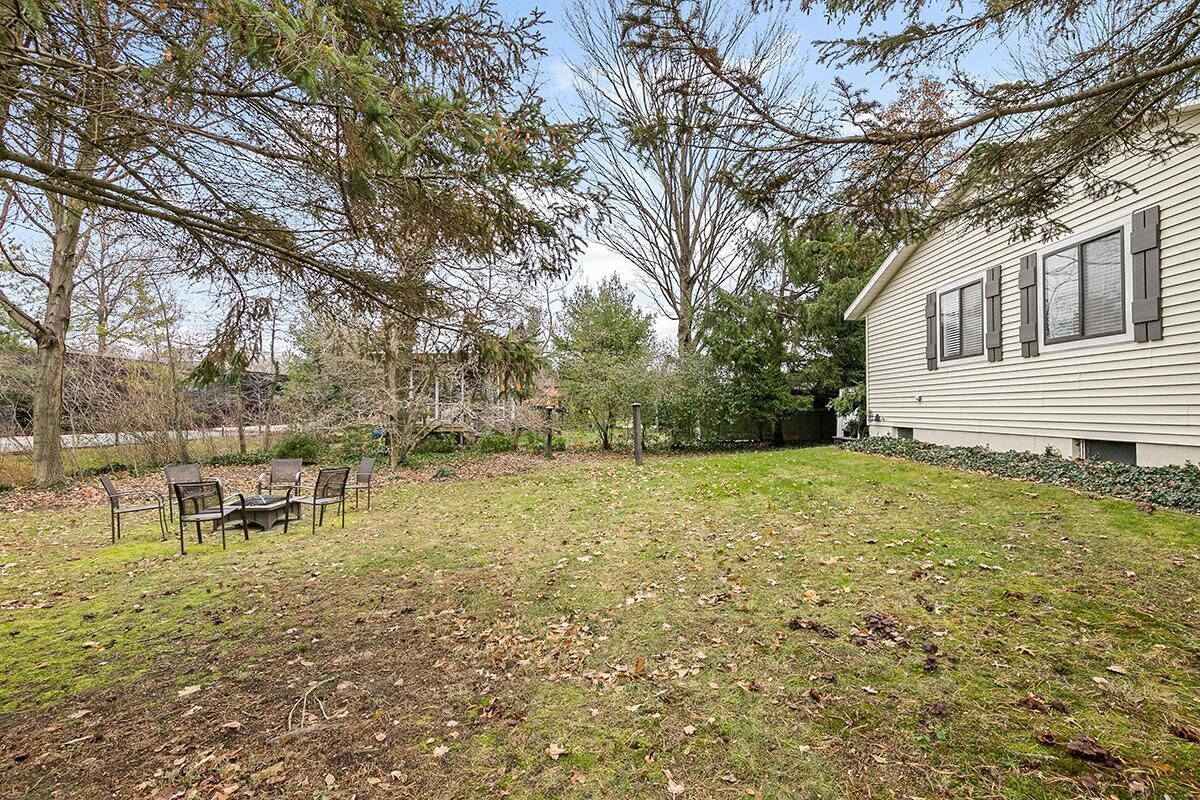 A backyard with a lawn, a wooden deck with chairs, and a house with shutters.