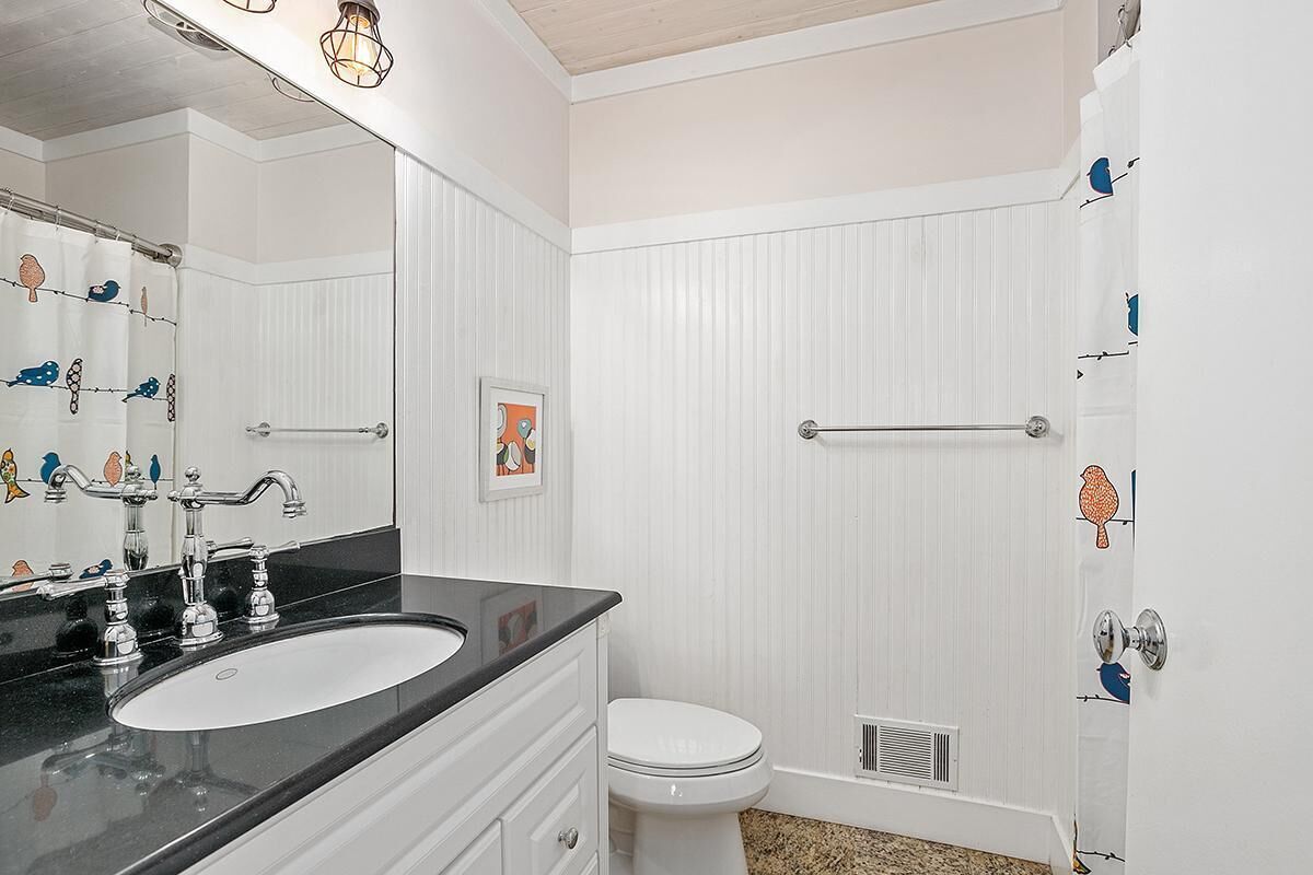 A bathroom with a white sink, two faucets, a toilet, and a shower with a white curtain.