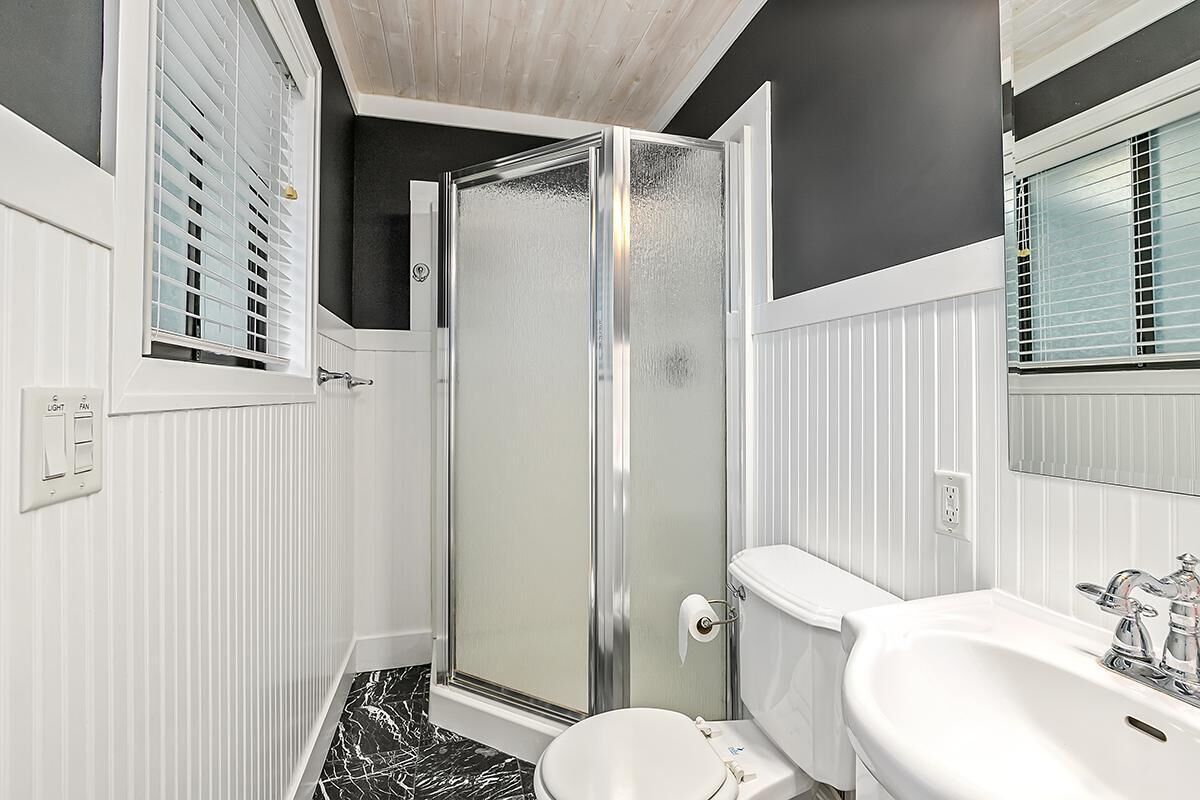 A bathroom with a glass-enclosed shower, a white toilet, and a sink with a mirror above it.