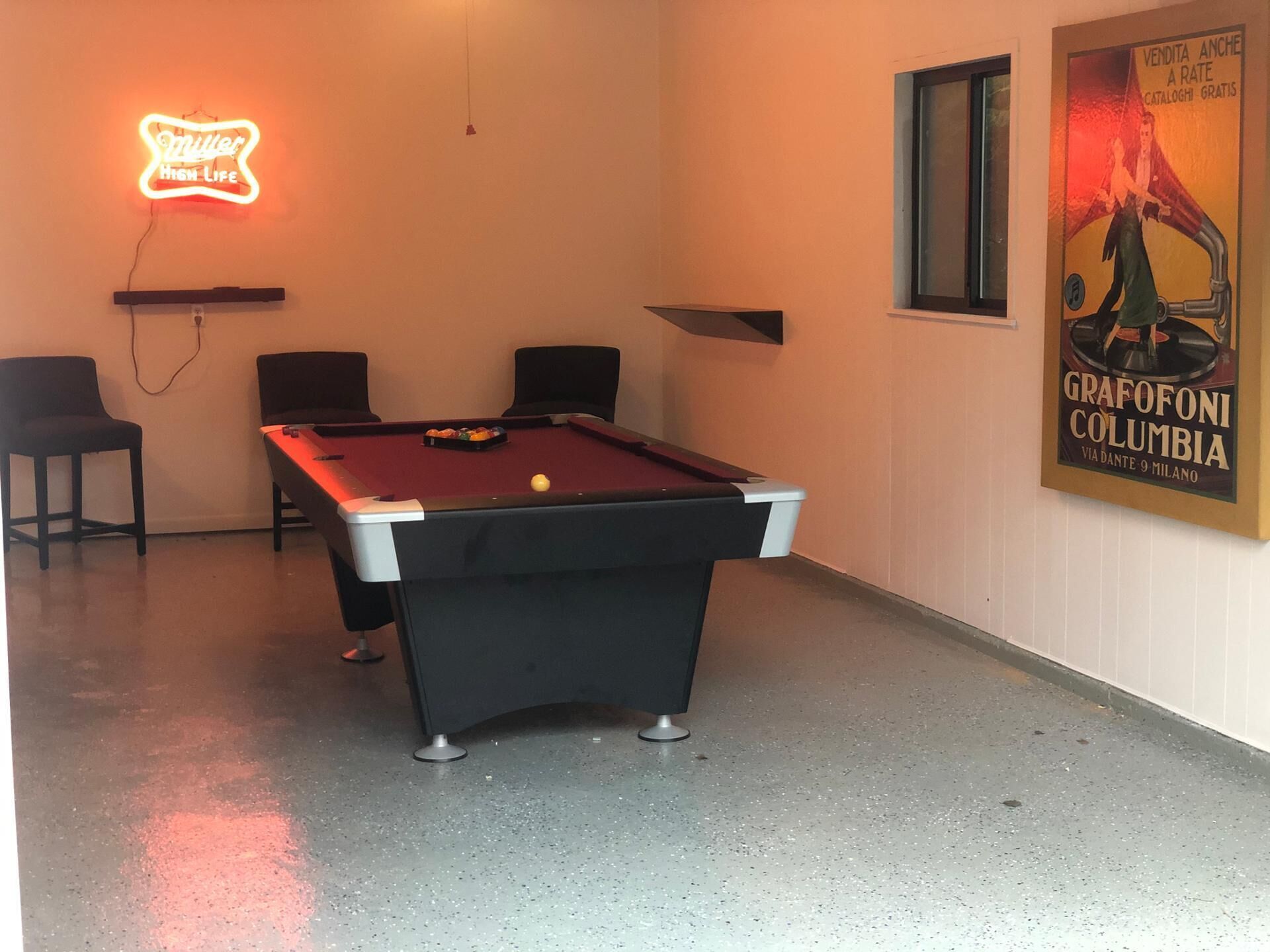 A pool table with chairs, a neon sign, and a poster on the wall.