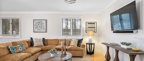 A living room with a sectional sofa, a round coffee table, and a TV mounted on the wall.