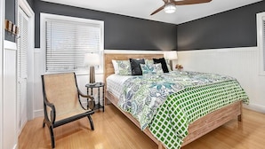 Une chambre à coucher comprenant un lit, une chaise, un ventilateur de plafond et une fenêtre avec des stores.