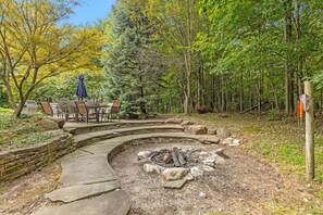 Un foyer circulaire en pierre, entouré d’un muret de pierre, avec un chemin sinueux également en pierre menant à un espace de détente comprenant des chaises et une table.